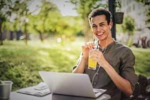 Happy young man drinking juice while working on laptop